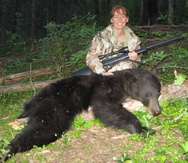 A woman sitting next to a bear with a rifle.
