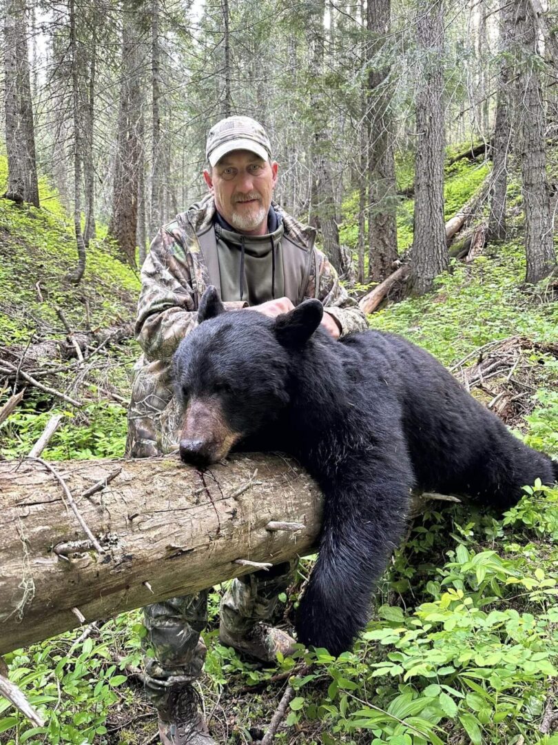 A man sitting on top of a log next to a bear.
