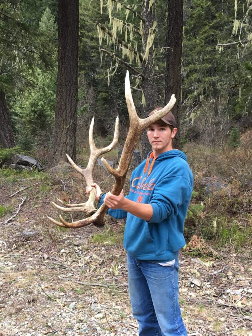 A man holding an antler in the woods.